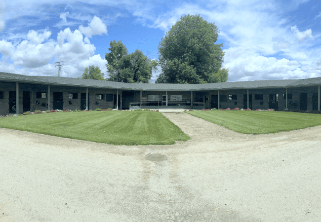 A panoramic view of the U-shaped concrete block stable complex at The Cole Ranch, featuring manicured green lawns and vibrant flower beds.